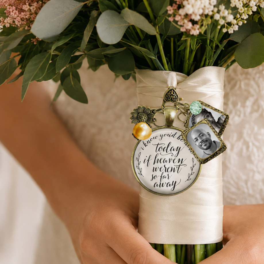 Handcrafted bridal bouquet memorial charm in vintage bronze featuring a heart photo frame, yellow sunflower accent, and scripted quote tag reading "I know you'd be here today if heaven weren't so far away" pinned to a wedding bouquet.