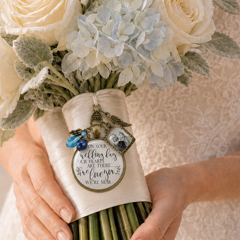 Bride holding a wedding bouquet wrapped in champagne ribbon adorned with a vintage bronze memorial charm featuring a custom grandparents photo frame, angel wing, blue crystal beads, and scripted quote: "On your wedding day our hearts are there... We love you, we're near."