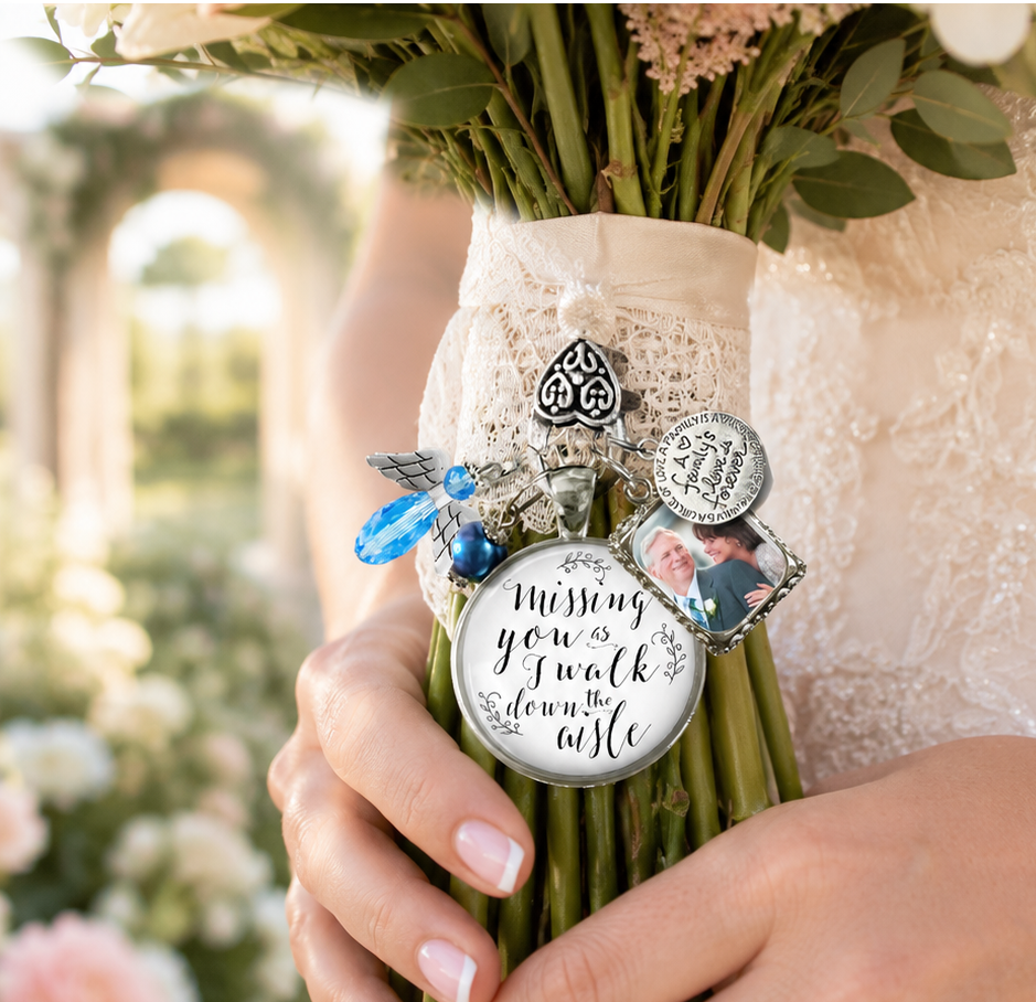 A close-up of a bouquet wrapped in a cream lace wristband, held by a person in a white lace dress. The bouquet is decorated with silver charms, including a round pendant that reads 'Missing you? I walk down the aisle.